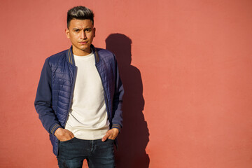 Young latin man posing with a red wall in the background. With copy space