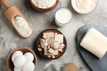 Pieces of compressed yeast and ingredients for dough on grey table, flat lay