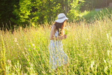 Happy young woman with long hair in hat and dress walking through the summer forest on a sunny day. Summer joy concept