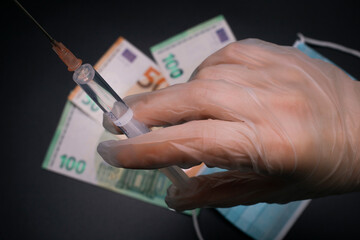Hand holds syringe with vaccine, cash on the background. Medical syringe with Covid-19 vaccine and money. Cost of coronavirus vaccine. 