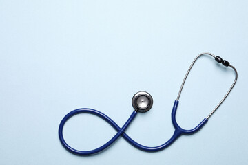 Stethoscope on light blue background, top view. Space for text