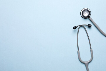 Stethoscope on light blue background, top view. Space for text