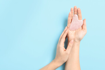 Woman with rose quartz gua sha tool on light blue background, closeup. Space for text