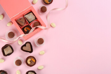 Fototapeta na wymiar Different delicious chocolate candies with box on light pink background, flat lay. Space for text