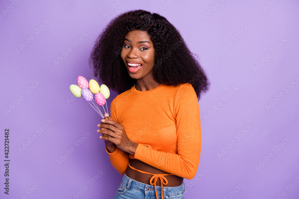 Sticker Photo of sweet shiny dark skin woman dressed orange holding easter eggs sticks isolated purple color background