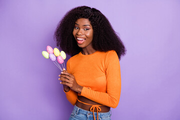 Photo of sweet shiny dark skin woman dressed orange holding easter eggs sticks isolated purple color background