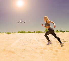 The plane flies in the sky under the sun and a sports girl runs on the sand in the desert. Exercise in nature