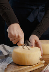 Obraz na płótnie Canvas Somebody hands cut a wheel of fresh homemade cheese on a wooden board