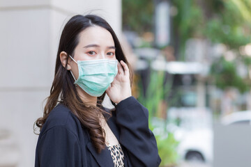 Asian beautiful woman in black coat is wearing a medical face mask to protect respiratory system from Coronavirus-19 (COVID-19) infection in health care,pollution PM2.5 and new normal concept..