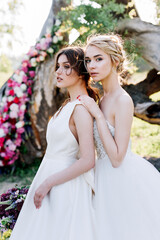 two girls in wedding dresses with bouquets on a background of flowers