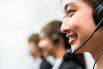 Side view of smiling woman consultant wearing microphone headset of customer support phone operator at workplace.