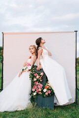 two girls in wedding dresses with bouquets on the background in the meadow