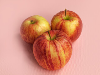 Three ripe apples of the gala variety lie on a pink background
