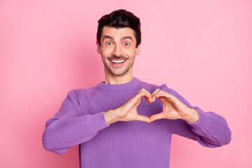 Portrait of attractive cheerful amorous guy showing heart symbol sign isolated over pink pastel color background
