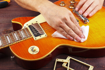 Guitar repairer wipes varnished surface of electric guitar with rag at workplace.