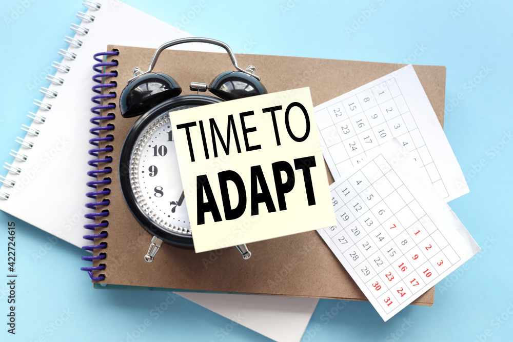 Poster time to adapt. text on the sticker attached to the alarm clock. alarm clock on notepad on blue backg