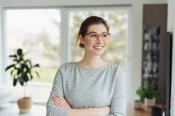 Happy young woman leaning on an interior wall smiling to herself