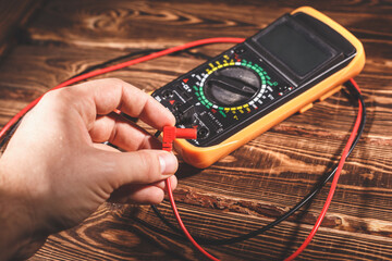 Multimeter and two test leads on a wooden background. A man's hand holds two test leads. A studio...