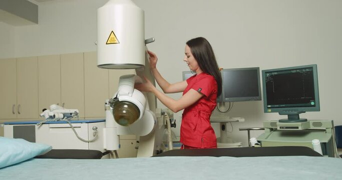 Portrait of young attractive woman doctor, standing near modern ultrasonic lithotripter while preparing for extracorporeal shock wave therapy in modern urology center. Ultrasonic lithotripter settings