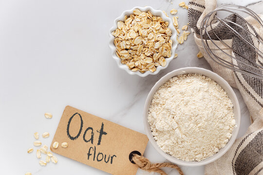 Oat flour and oat flakes on white marble background with a brown tag. Concept of gluten free cooking and baking