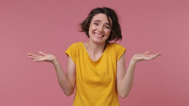 Brunette fun confused shy shamed short hairdo young woman 20s wears casual yellow t-shirt look camera spreading hands say oops ouch oh i am so sorry isolated on pastel pink background studio portrait