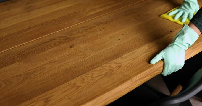 Unrecognizable female in latex gloves with microfiber rag cleaning the wooden table surface , desk at home, woman wife do daily house cleaning routine.
