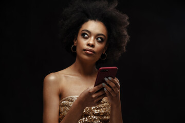 Pensive young african woman in dress holding mobile phone