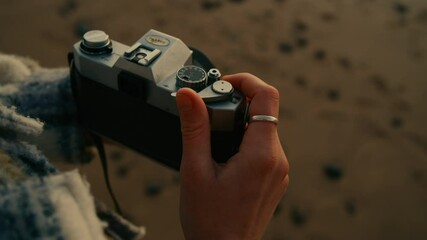 Close up on woman rewind film to next frame on old vintage camera. Millennial hipster photography hobby. Cinematic film photocamera in soft sunset light at beach