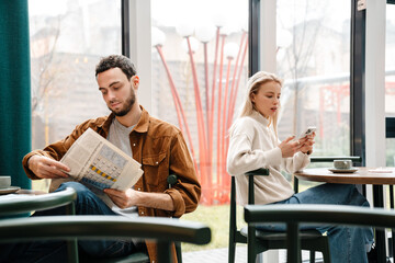 Focused man and woman using cellphone and reading newspaper