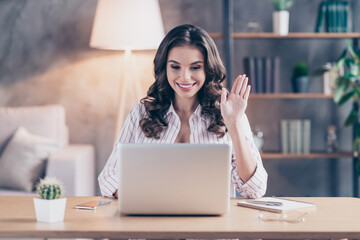 Photo of sweet friendly young lady wear white shirt waving arm talking modern gadget sitting table indoors inside room home