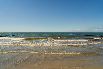 Fototapeta na wymiar Wellen am Strand im Ostsee Meer vor blauem Himmel