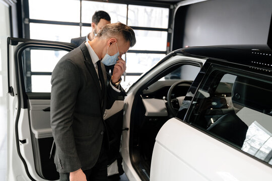 Mid White Manager In Face Mask Showing Car To Customer In Showroom