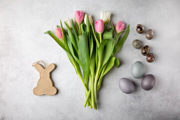 Colorful Easter eggs, decorative bunny, and tulip flowers on gray background. Happy Easter concept.  Top view, flat lay.