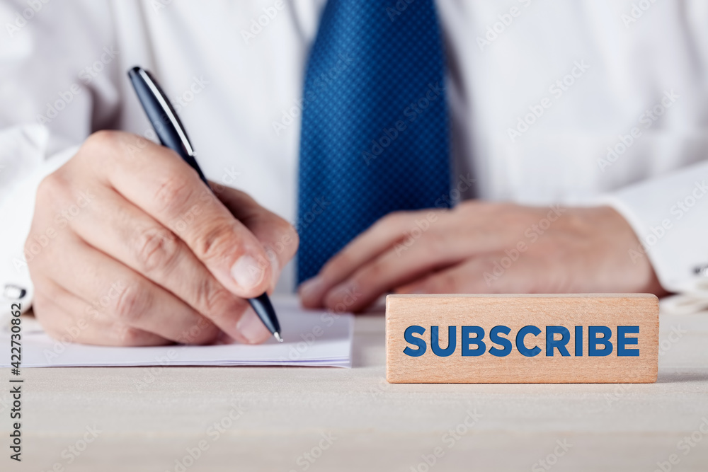 Poster the word subscribe written on a wooden block in front of a businessman filling a form at the backgro