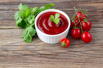 White bowl of tomato sauce with parsley and tomato. Ketchup on natural wooden background