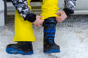 The snowboarder laces up the special shoes. Sunny winter day. Front view.