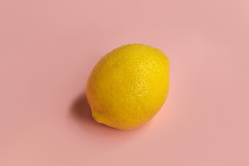 One whole lemon lies in the center on a pink background