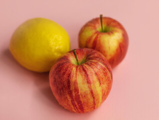Two ripe gala apples and one lemon lie in the center on a pink background