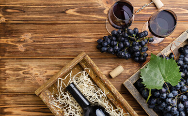 Red Wine composition on brown wooden table. Top view. Red wine bottle corkscrew corks wine glasses black ripe grapes in box on wooden table. Flat lay copy space banner