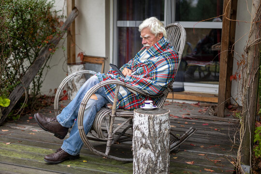 Senior man reading a book on his e-book reader when sitting in the rocking chair.  Portrait of a happy, retired man reading a book on his device.
