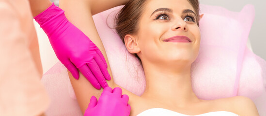 Obraz na płótnie Canvas Beautiful young caucasian smiling woman receiving waxing her armpit by hands of a beautician in a medical spa