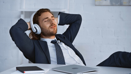 smiling businessman listening music in wireless headphones while resting in office