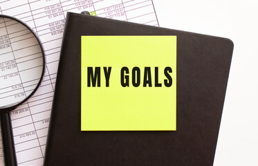 MY GOALS text on a sticker on your desktop. Diary and magnifier.