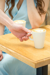 Hand of waiter puts a cup of coffee latte on the wooden table in a cafe