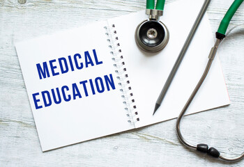 MEDICAL EDUCATION is written in a notebook on a wooden table next to stethoscope.