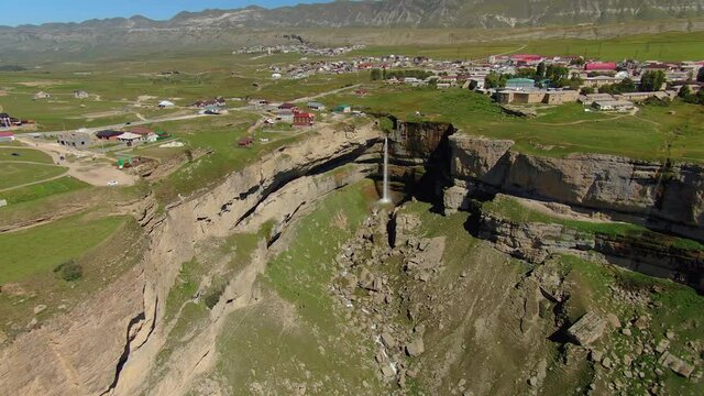 Aerial sideways beautiful Tobot waterfall Dagestan, highest Caucasus fall. Falls powerful from cliff into deep gorge. Old authentic village aul on edge. Russia unusual national landmark. Mountains