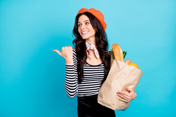 Photo of young girl happy smile hold paper bag buy food indicate thumb empty space advice ad isolated over blue color background - Powered by Adobe