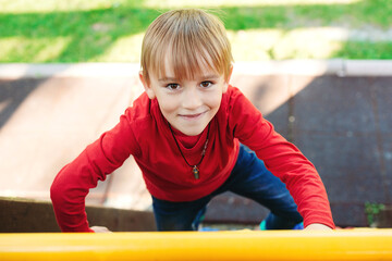 Fototapeta na wymiar Portrait of happy child outdoors. Kid climbing on the wooden wall. Happy summer vacation.