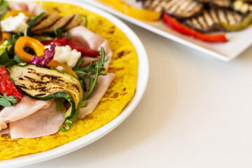 Turmeric flatbread with ham cheese and grilled vegetables on a white background.