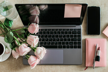 Female workspace laptop, pink rose bouquet, notebook and coffee cup top view